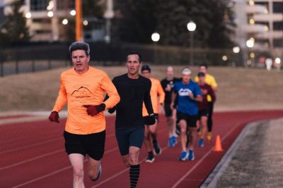 A ilne of eight runners, led by a man in a fluorescent orange shirt, chases down the Virginia Tech track.